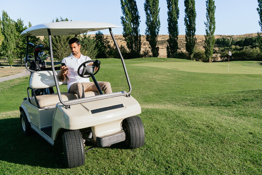 Golfer chatting on smartphone in golf cart in countryside field