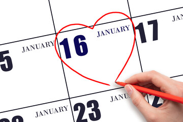 A woman's hand drawing a red heart shape on the calendar date of 16 January. Heart as a symbol of...