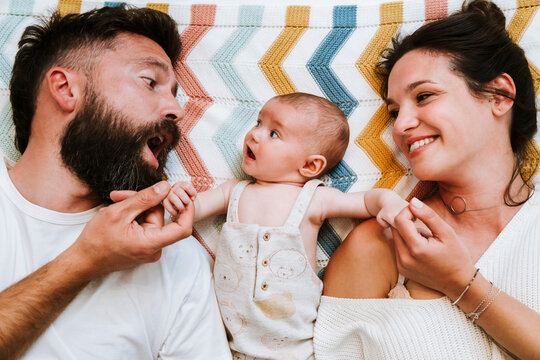 Happy parents having fun while relaxing with infant together on bed