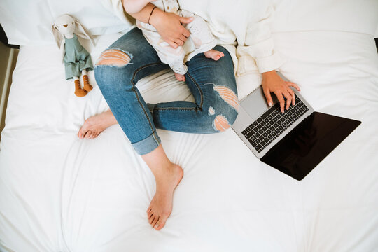 Anonymous mother using computer with interest while chilling with infant together at home