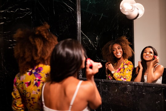 Cheerful young diverse female friends refresh makeup in bathroom