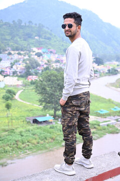 an indian boy standing along side the holy river with blurred hills in background.