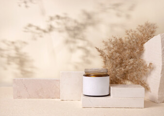 Glass cosmetic jar with blank label on stones near pampas grass close up, Mockup
