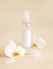 Fototapeta na wymiar Spray dispenser bottle near white orchid flowers on light beige close up. Mockup