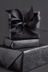 Wrapped Black Gift Boxes with a ribbon bow on black close up. Black Friday concept