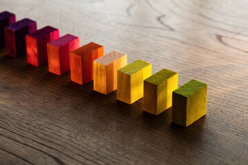 Colored wooden blocks aligned on an old vintage wooden table. Yellow to orange color in warm lighting.  variation, selection, or diversity concept. Plenty of copy space for cover, header usage.