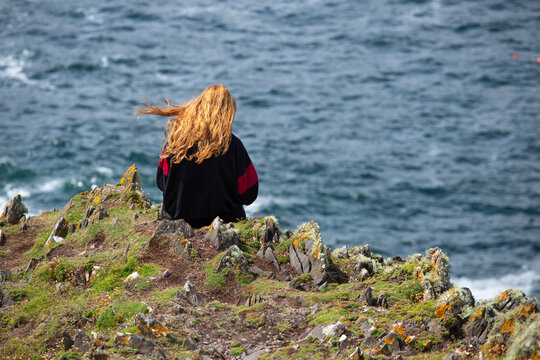 une jolie jeune fille irlandaise aux longs cheveux roux est assise sur un rocher face à la mer dans le Connemara