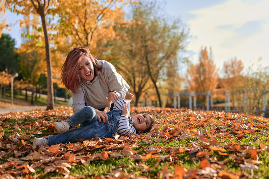 Happy mother tickling little son in park in fall