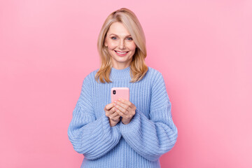 Fototapeta premium Photo of cute mature blond lady hold telephone wear blue sweater isolated on pink color background