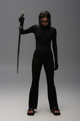 full length of brunette asian woman in sunglasses and black outfit holding katana on grey. © LIGHTFIELD STUDIOS