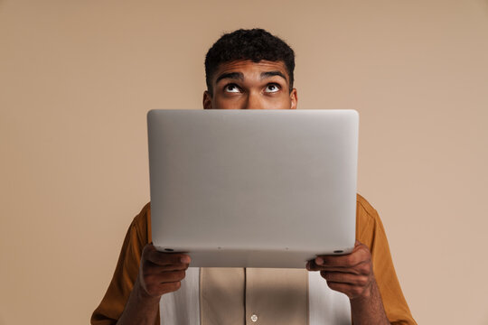Young handsome african man peeking out from behind a laptop
