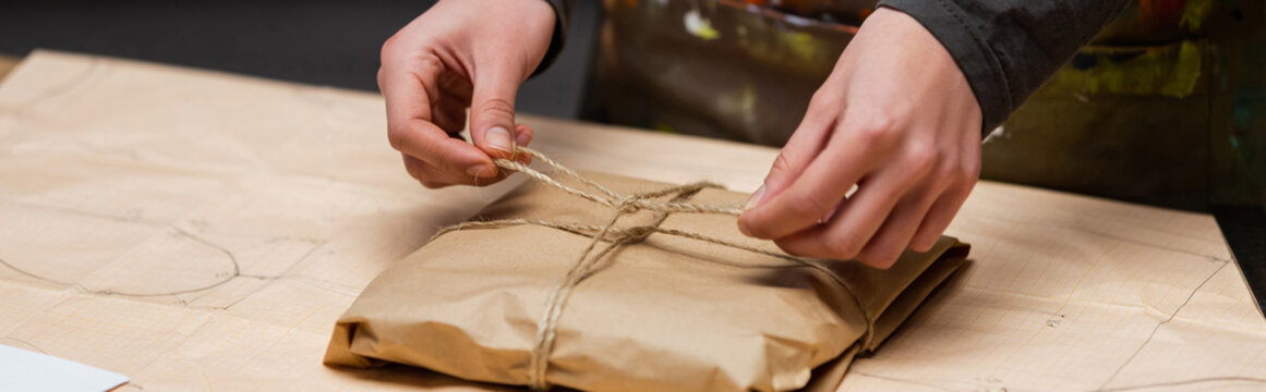 Cropped view of african american designer tying twine on package in workshop, banner.