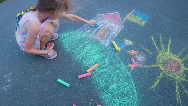 Ukrainian girl child draws children's drawings with chalk on the pavement.