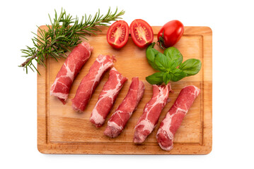 Raw pork neck steak rolls (coppa) on wooden cutting board with rosemary, chopped cherry tomatoes and basil leaves isolated on white, top view, clipping path