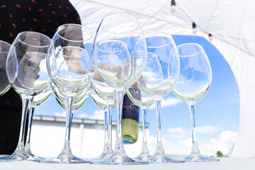 Empty wine glasses stand on a white tablecloth against a blue sky. Preparation for a banquet or buffet