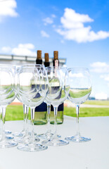 Empty wine glasses stand on a white tablecloth against a blue sky. Preparation for a banquet or buffet