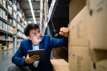 Portrait of an employee or worker working in a warehouse. An Asian male employee uses a digital tablet to check inventory in a large warehouse. Distribution center. Logistics and export business.