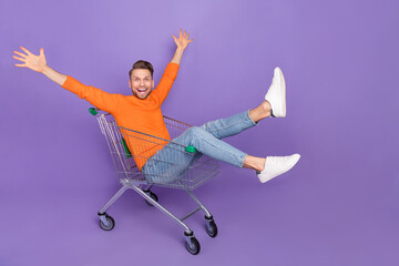 Full body photo of energetic laughing man have fun sitting in pushcart go shopping isolated on...