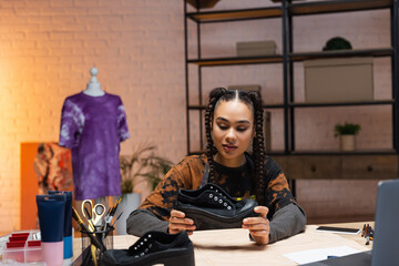 African american craftswoman holding shoe near sewing pattern and devices.