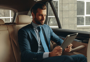 Seriously business man looking to the screen of modern device in auto