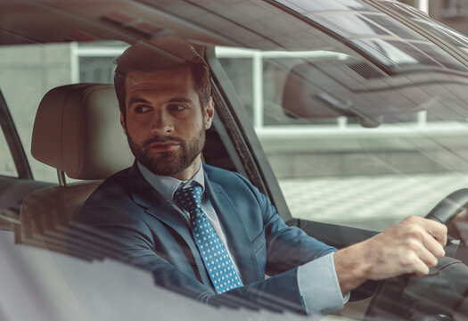 Handsome seriously businessman in suit sitting in salon of his car