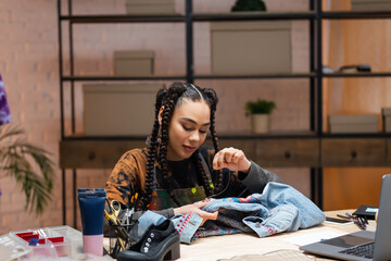 African american designer embroidering denim jacket near devices in workshop.