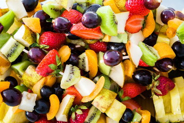 Colorful mixed fruit salad served on barbecue sticks. Selective focus