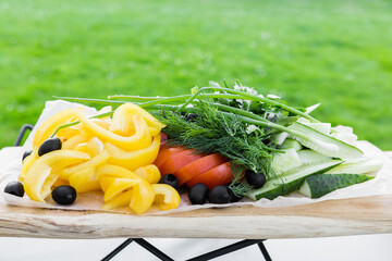 Vegetable plate on a wooden dish against the background of bright green grass. Healthy food concept