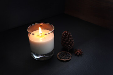 burning luxury aromatic scented candle glass on the black table with spices on background of old...