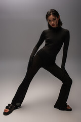 full length of young asian woman in total black outfit posing on grey.
