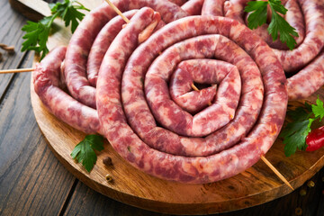 Raw spiral pork sausages. Fresh pork sausages tasty twisted spiral for bbq on white stand with spices and herbs for Octoberfest party dinner on old wooden background. Top view. Oktoberfest set.
