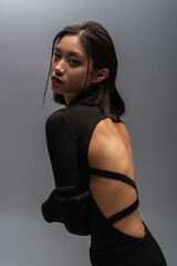 stylish and young asian model in black outfit looking at camera isolated on grey.