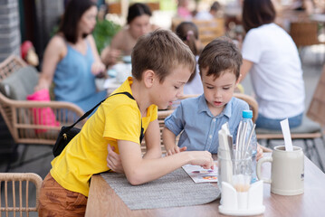 Two little boys in a cafe look at the menu and choose what to eat.