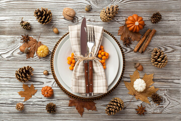 Thanksgiving day concept.. Top view photo of table setting plate knife fork napkin rowan small pumpkins pine cones acorns anise nut cinnamon sticks maple leaves isolated grey wooden table background