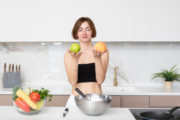 Young slender and fit woman in sportswear holding apple and peach in the kitchen. Cooking healthy food concept