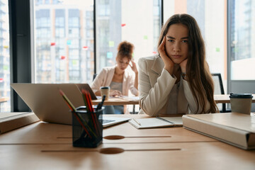 Portrait of pensive woman sitting at table with open laptop