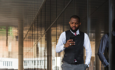 Portrait of an afro american businessman in a suit using the phone on the background of a modern building exterior. Business style outdoor