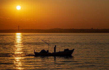 Fisherman silhouette going fishing with boat at sunset