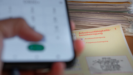 Telefonische Verlängerung der Krankschreibung/ digitaler Krankenschein: Hand wählt Nummer auf Smartphone und Arbeitsunfähigkeitsbescheinigung, digitaler Krankenschein
