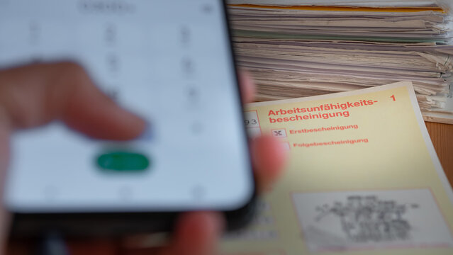 Telefonische Verl&auml;ngerung der Krankschreibung/ digitaler Krankenschein: Hand w&auml;hlt Nummer auf Smartphone und Arbeitsunf&auml;higkeitsbescheinigung, digitaler Krankenschein