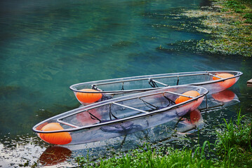 Two transparent boats on the lake near the shore .