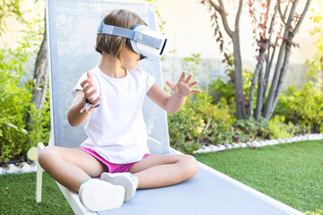 Little girl with virtual reality glasses, looking to the right, trying to touch something in a...