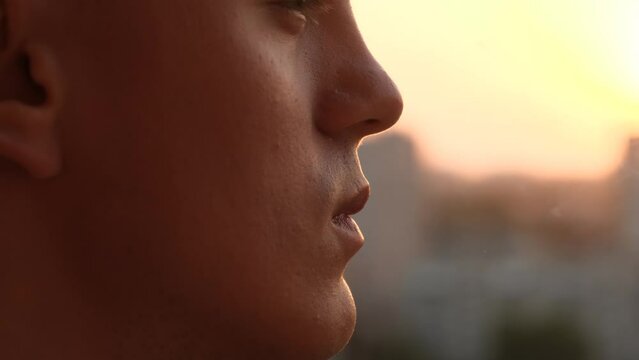 Young man smoking a cigarette at sunset, closeup