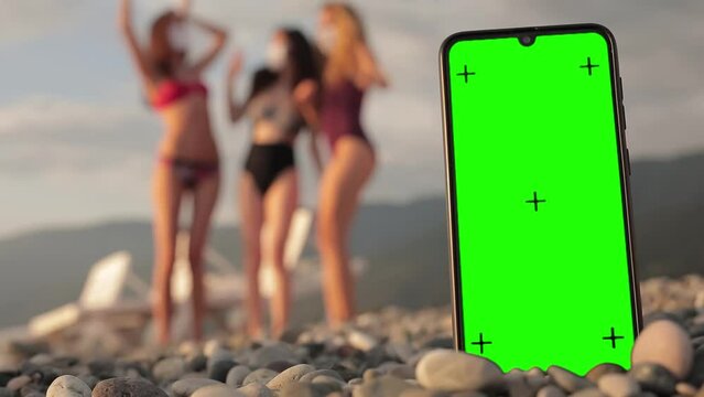 Phone With A Green Screen And Tracking Dots On The Beach, Three Multi-racial Girls In Swimsuits Dancing In The Background. Chromakey