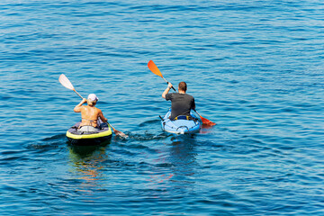 A man and a woman aboard their kayak, paddling in the blue Mediterranean sea, on a sunny summer day. Gulf of La Spezia, Liguria, Italy, southern Europe.