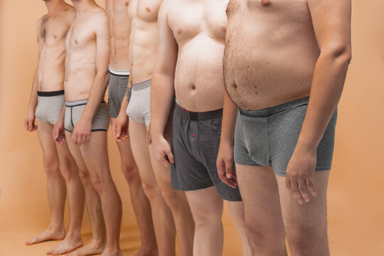 Cropped image of male bodies in boxers panties standing together at studio photo shoot. Fun, joy, body positive and creativity