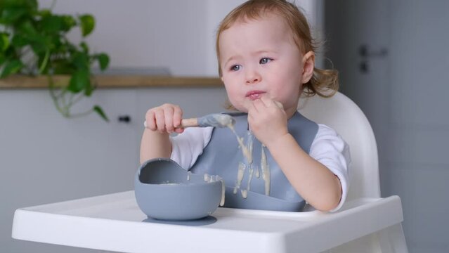 4K video Cute baby sitting in highchair self-feeding using hand. Enjoying eating. Exploring food through touch, taste, sight and smell
