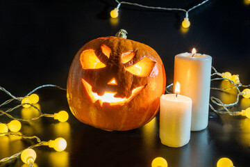 Halloween carved pumpkin. The smiling face of Jack O Lantern. Illuminated by a burning candle inside the scary Jack Lantern. Pumpkin decoration. Happy Halloween. yellow lanterns on black background