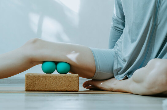Person doing self myofascial release of hamstrings with two massage balls on cork block. 