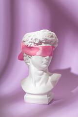 An artificial sculpture of the head of David with his eyes tied with a pink ribbon on a purple...